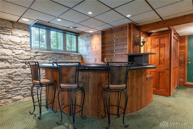 bar featuring a drop ceiling, wooden walls, and carpet flooring