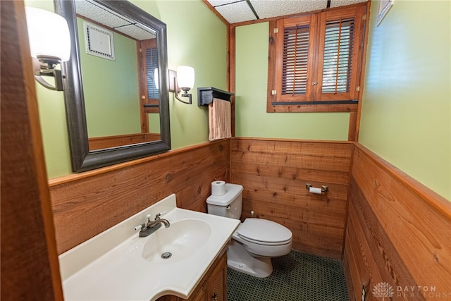 bathroom featuring tile patterned flooring, toilet, wooden walls, and vanity