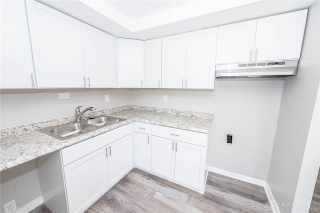 kitchen with light stone countertops, light hardwood / wood-style floors, white cabinetry, and sink