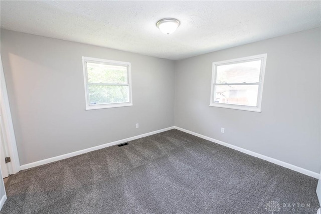 empty room with a textured ceiling and dark colored carpet