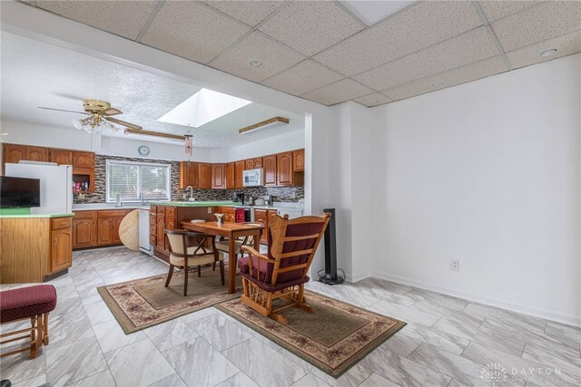 kitchen featuring backsplash, a skylight, a drop ceiling, white appliances, and ceiling fan