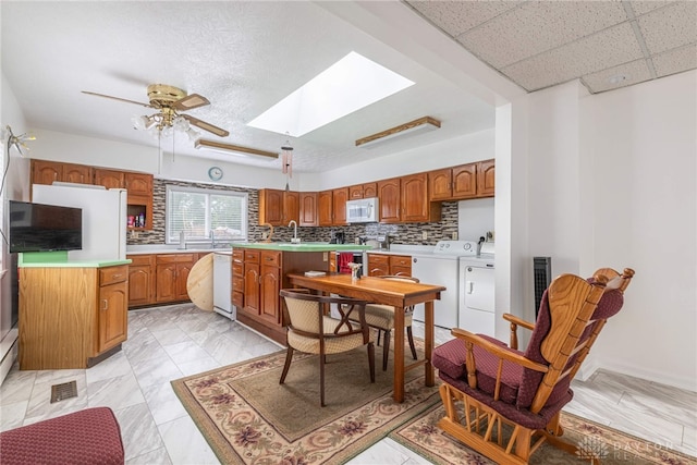 kitchen with a skylight, ceiling fan, washing machine and dryer, white appliances, and decorative backsplash