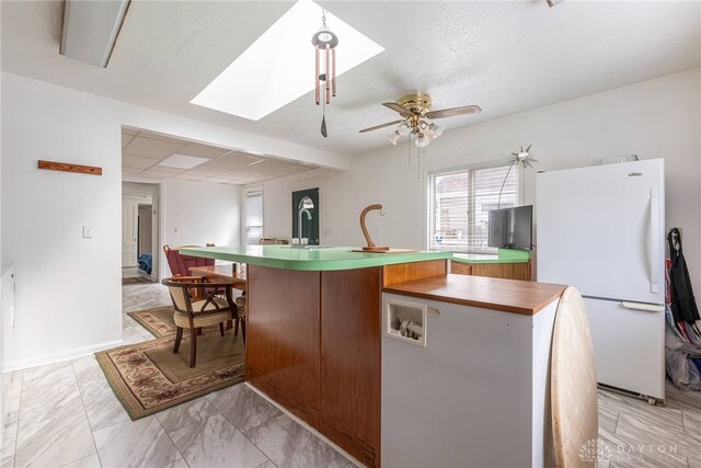 kitchen with a skylight, a textured ceiling, a kitchen island with sink, ceiling fan, and white refrigerator