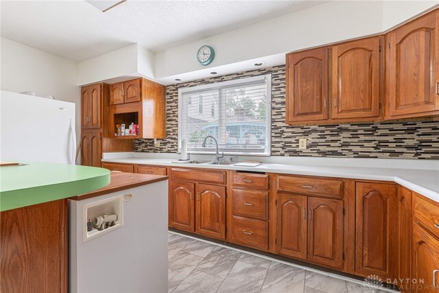 kitchen with a textured ceiling, white fridge, sink, and tasteful backsplash