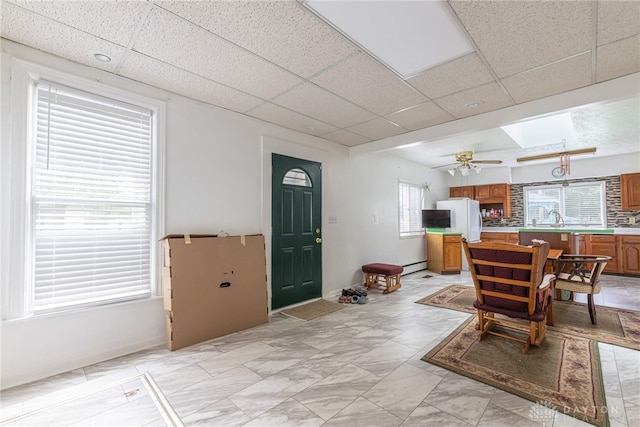 interior space with ceiling fan, a drop ceiling, a baseboard radiator, white refrigerator, and backsplash