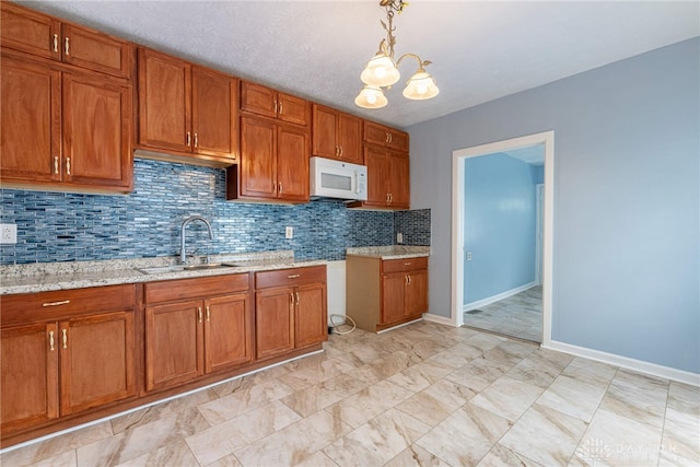 kitchen with sink, tasteful backsplash, a chandelier, hanging light fixtures, and light stone countertops