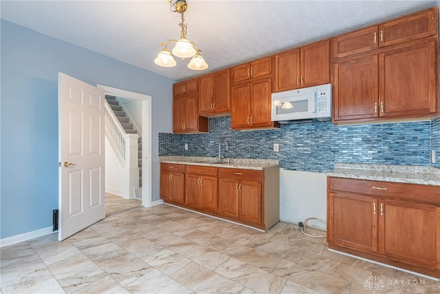 kitchen featuring pendant lighting, sink, decorative backsplash, light stone counters, and an inviting chandelier