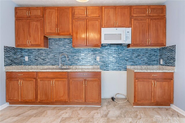 kitchen featuring decorative backsplash, sink, and light stone counters