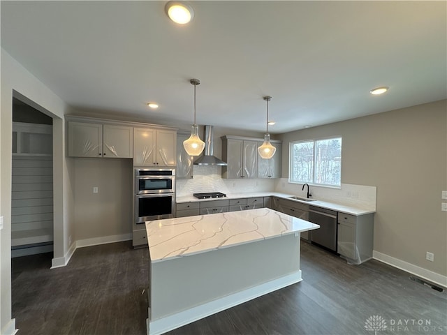 kitchen featuring sink, stainless steel appliances, decorative light fixtures, wall chimney exhaust hood, and a kitchen island