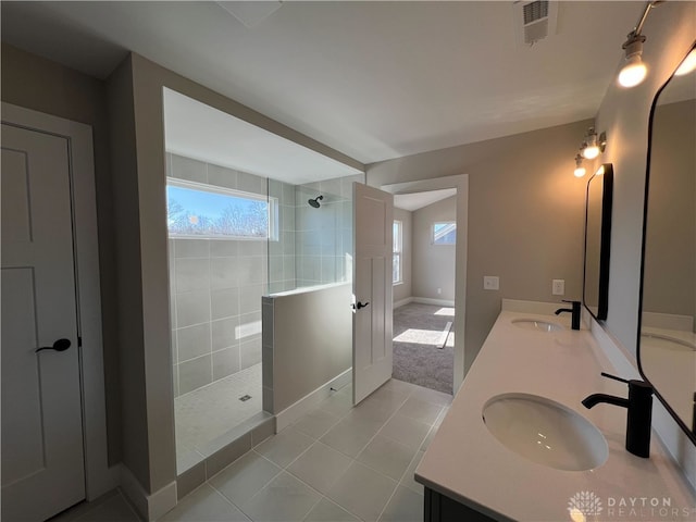 bathroom with tile patterned floors, a healthy amount of sunlight, vanity, and a tile shower