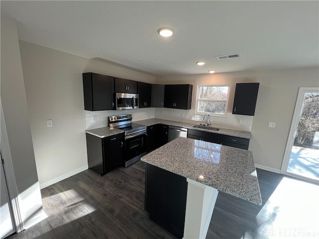 kitchen with light stone counters, stainless steel appliances, sink, a center island, and dark hardwood / wood-style floors