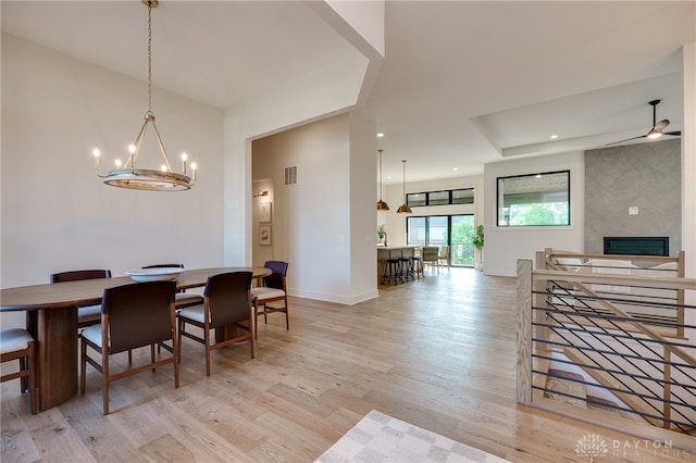 dining room with light hardwood / wood-style flooring, a fireplace, and ceiling fan with notable chandelier