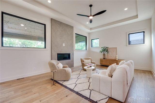 living room featuring light hardwood / wood-style floors, a tray ceiling, a large fireplace, and ceiling fan