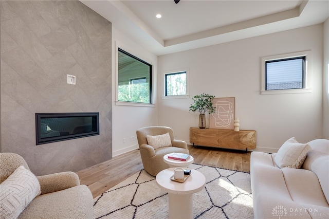 living room with tile walls, a high end fireplace, light hardwood / wood-style flooring, and a tray ceiling