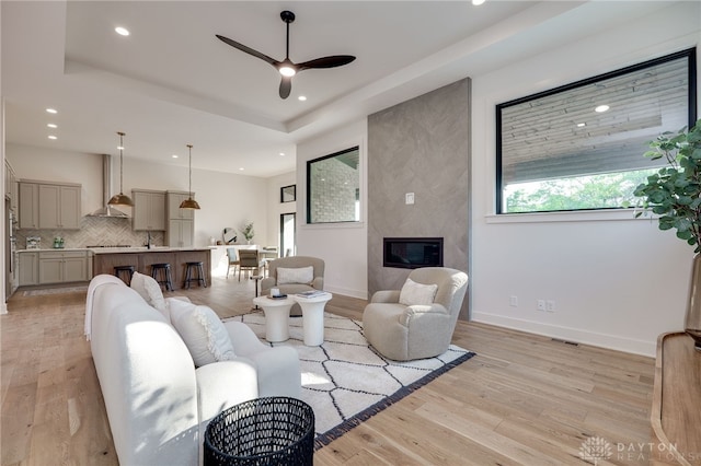 living room with ceiling fan, a tray ceiling, light wood-type flooring, and a fireplace