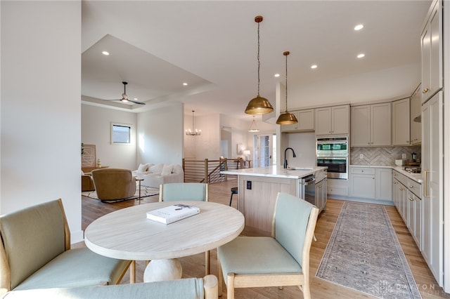 dining room featuring sink, light wood-type flooring, and ceiling fan with notable chandelier