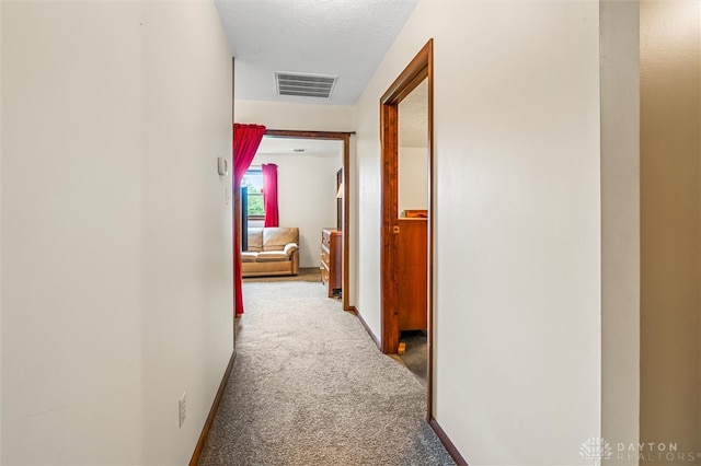 hallway featuring light carpet and a textured ceiling