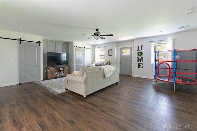 living room featuring a barn door, ceiling fan, and dark wood-type flooring