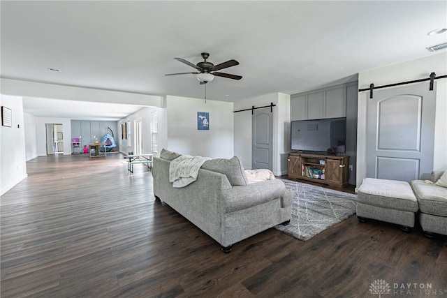 living room with ceiling fan, a barn door, and dark hardwood / wood-style flooring