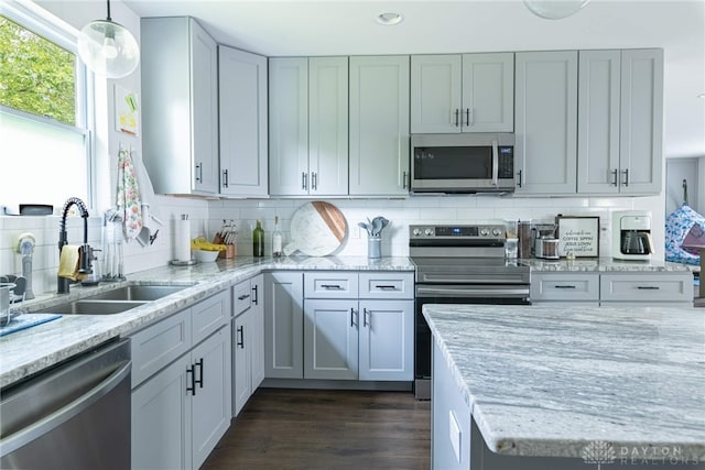 kitchen featuring dark wood-type flooring, hanging light fixtures, appliances with stainless steel finishes, tasteful backsplash, and light stone counters