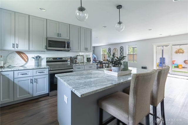 kitchen with dark wood-type flooring, hanging light fixtures, stainless steel appliances, tasteful backsplash, and light stone counters