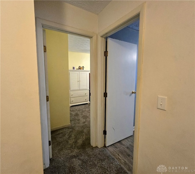 hallway featuring dark colored carpet and a textured ceiling