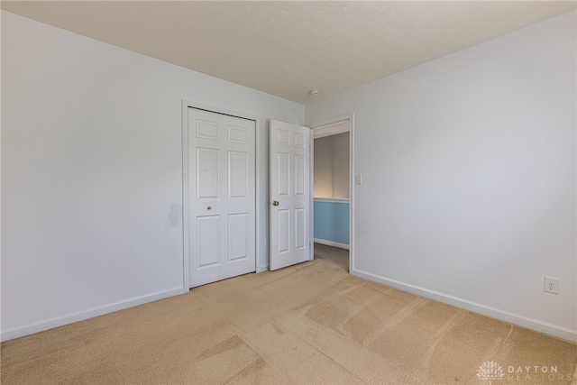 unfurnished bedroom with light carpet, a closet, and a textured ceiling