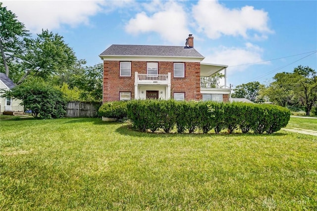back of property with a chimney, fence, brick siding, a balcony, and a lawn
