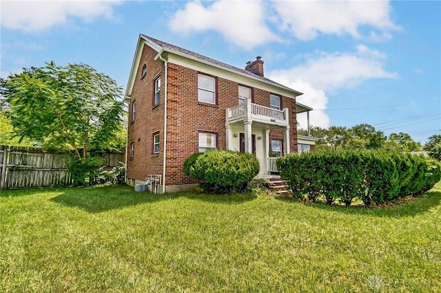 exterior space with brick siding, a balcony, a chimney, fence, and a front yard