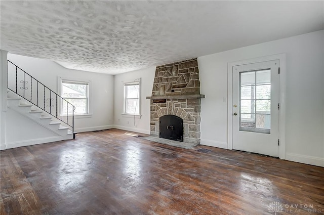 unfurnished living room with stairs, wood finished floors, a textured ceiling, a stone fireplace, and baseboards