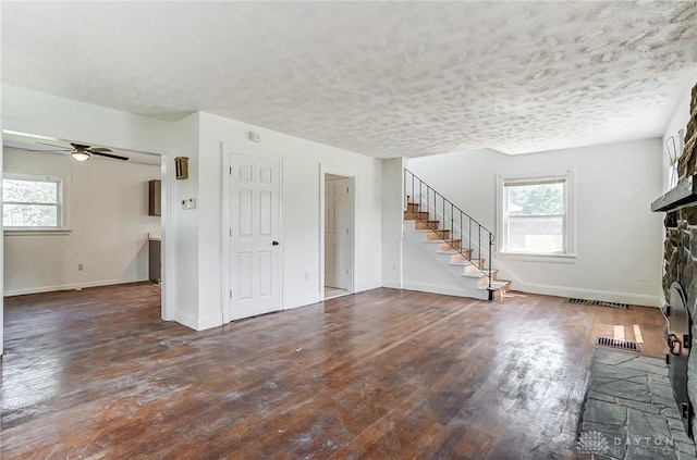 unfurnished living room featuring dark wood-type flooring, a stone fireplace, stairway, and a textured ceiling