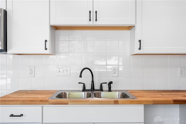 kitchen with decorative backsplash, white cabinetry, wooden counters, and sink