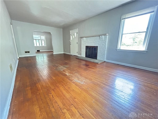 unfurnished living room with wood-type flooring, a brick fireplace, and plenty of natural light