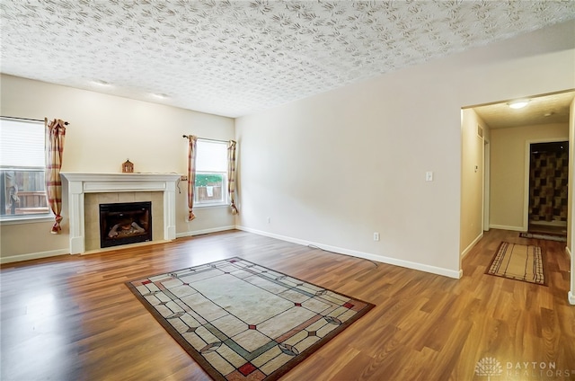 unfurnished living room with a tiled fireplace, hardwood / wood-style floors, and a textured ceiling