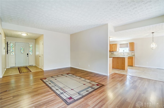 unfurnished living room featuring sink, a textured ceiling, and light hardwood / wood-style flooring