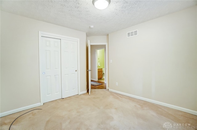 unfurnished bedroom featuring a closet, light colored carpet, and a textured ceiling