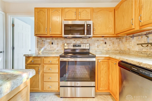 kitchen featuring backsplash, light stone countertops, light tile patterned floors, and appliances with stainless steel finishes