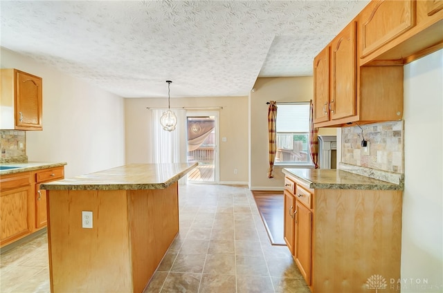 kitchen featuring backsplash, a textured ceiling, a chandelier, a center island, and hanging light fixtures