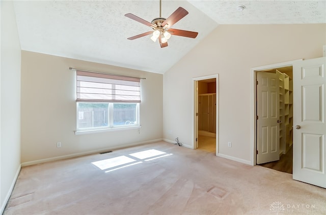 unfurnished bedroom featuring lofted ceiling, a walk in closet, ceiling fan, a textured ceiling, and light colored carpet