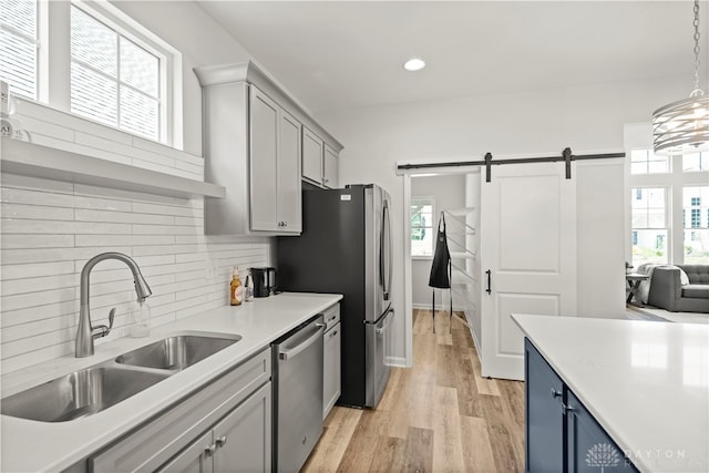 kitchen with light hardwood / wood-style flooring, appliances with stainless steel finishes, a barn door, tasteful backsplash, and sink