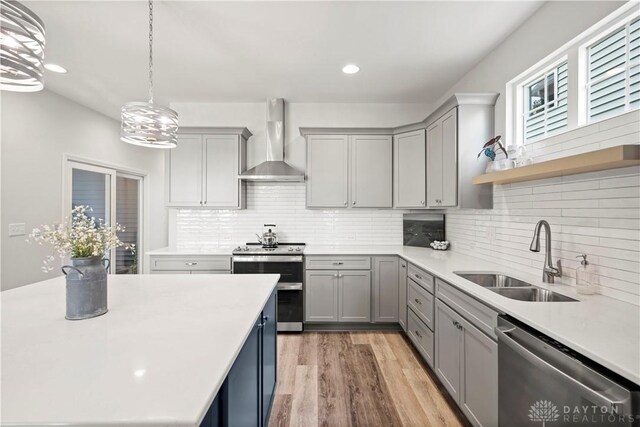 kitchen featuring stainless steel appliances, wood-type flooring, sink, tasteful backsplash, and wall chimney range hood