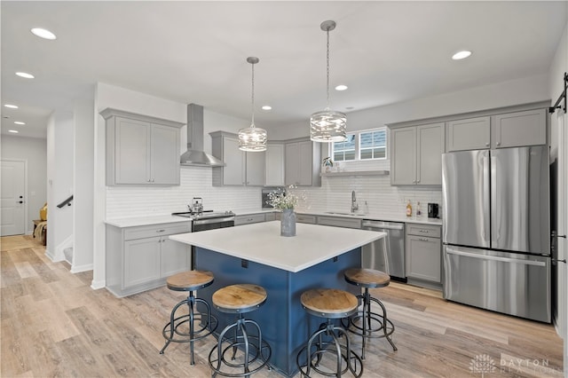 kitchen with appliances with stainless steel finishes, light wood-type flooring, sink, tasteful backsplash, and wall chimney exhaust hood