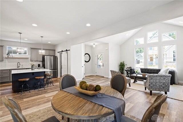 dining room featuring light wood-type flooring, a barn door, sink, and vaulted ceiling