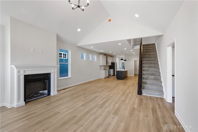 unfurnished living room featuring a notable chandelier, sink, high vaulted ceiling, and light hardwood / wood-style flooring