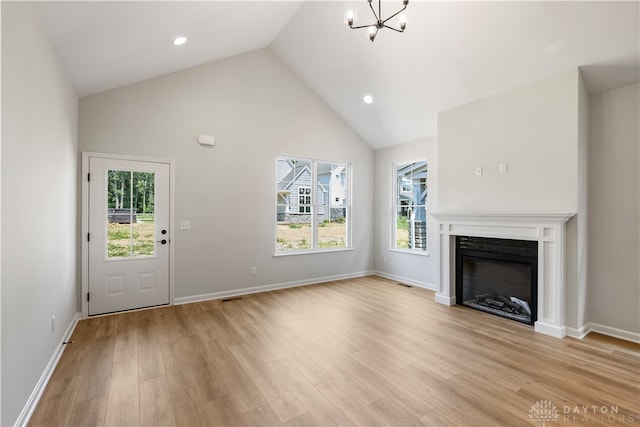 unfurnished living room with light wood-type flooring, high vaulted ceiling, and an inviting chandelier