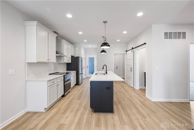 kitchen with tasteful backsplash, appliances with stainless steel finishes, light hardwood / wood-style flooring, white cabinets, and a barn door