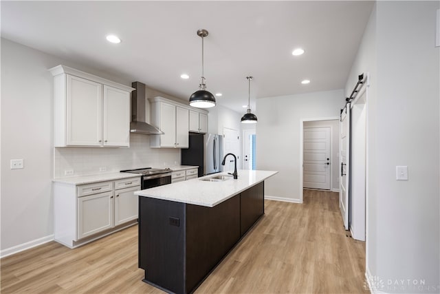 kitchen featuring stainless steel appliances, wall chimney range hood, a barn door, light hardwood / wood-style floors, and tasteful backsplash