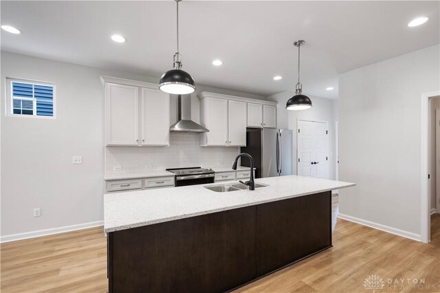 kitchen featuring stainless steel appliances, light hardwood / wood-style floors, backsplash, sink, and wall chimney exhaust hood