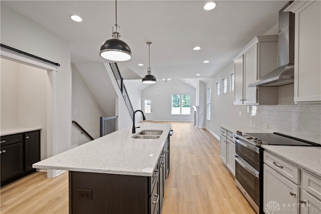 kitchen featuring light hardwood / wood-style flooring, wall chimney range hood, a center island with sink, and range with two ovens