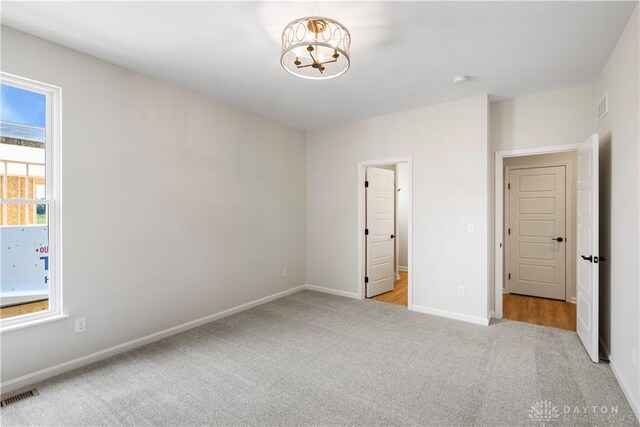 unfurnished bedroom with light colored carpet, multiple windows, and an inviting chandelier